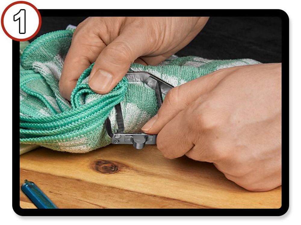 Hand umfasst die alte Klinge des TURBO Schälers mit einem Geschirrtuch zum Schutz