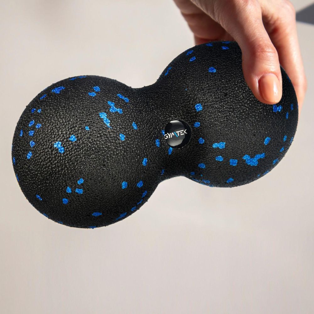 Eine Hand hält einen schwarz-blauen Duoball von GYMTEK zur Massage