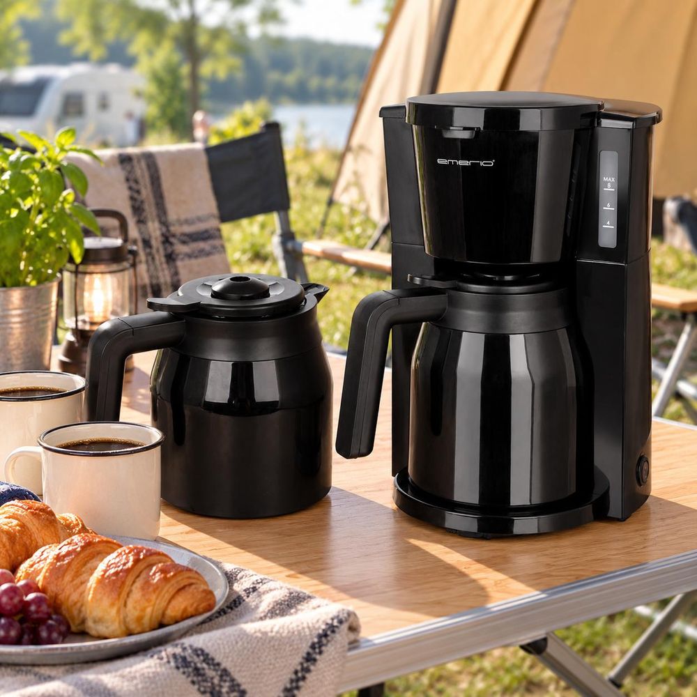 Filterkaffeemaschine mit Thermokannen auf einem Campingtisch vor einem Zelt.