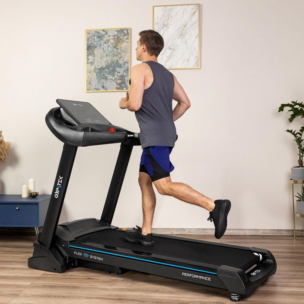 Mann joggt auf einem schwarzen Laufband mit blauen Details und "FLEX SYSTEM" im Wohnzimmer