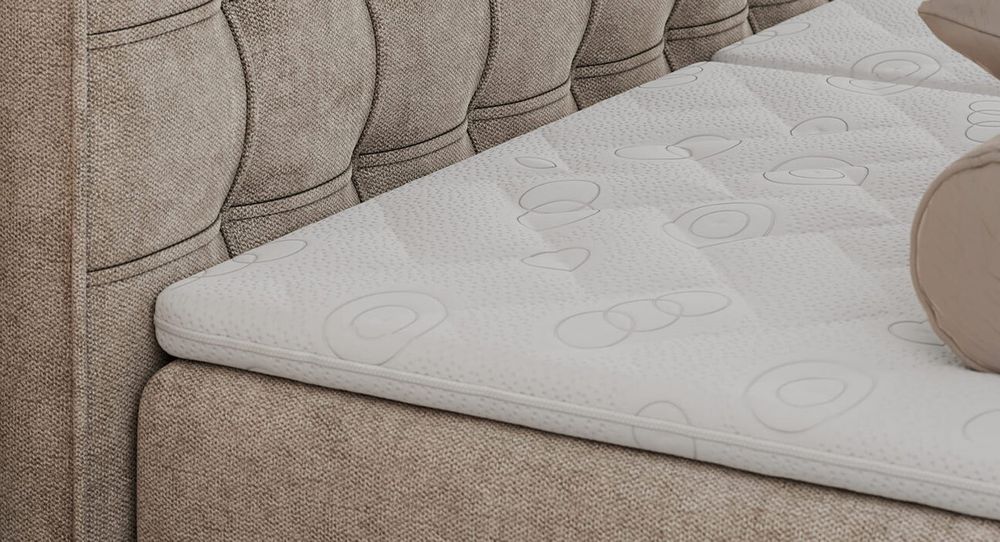 Gestepptes Kopfteil eines beige Bettes. Eine Topper-Matratze liegt auf dem Bett