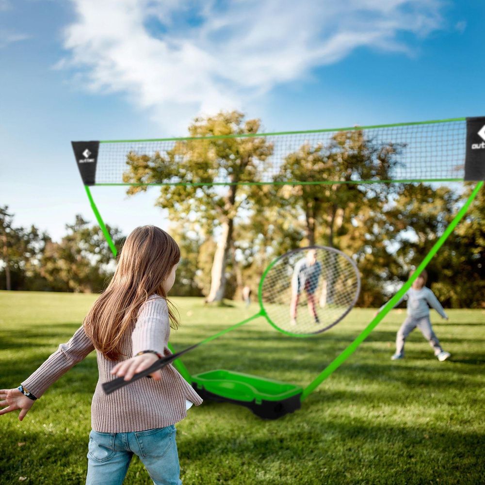 Mädchen spielt Badminton im Park, im Hintergrund Netz und andere Kinder