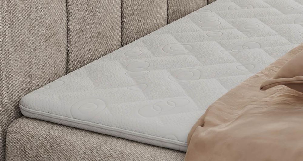 Gestepptes Kopfteil eines beige Bettes. Eine Topper-Matratze liegt auf dem Bett
