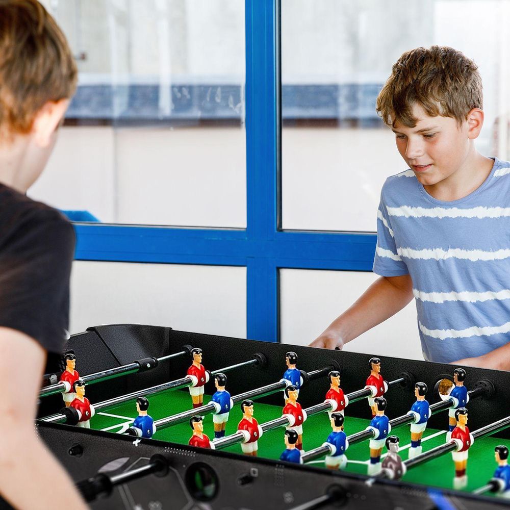 Zwei Jungen spielen begeistert Tischfußball am Kicker mit blauen und roten Figuren