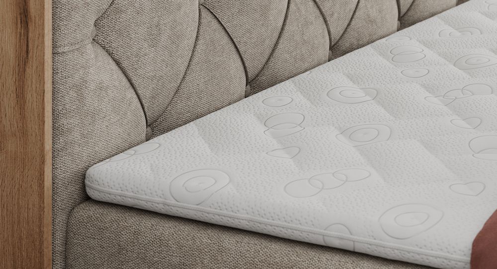 Gestepptes Kopfteil eines grau Bettes. Eine Topper-Matratze liegt auf dem Bett