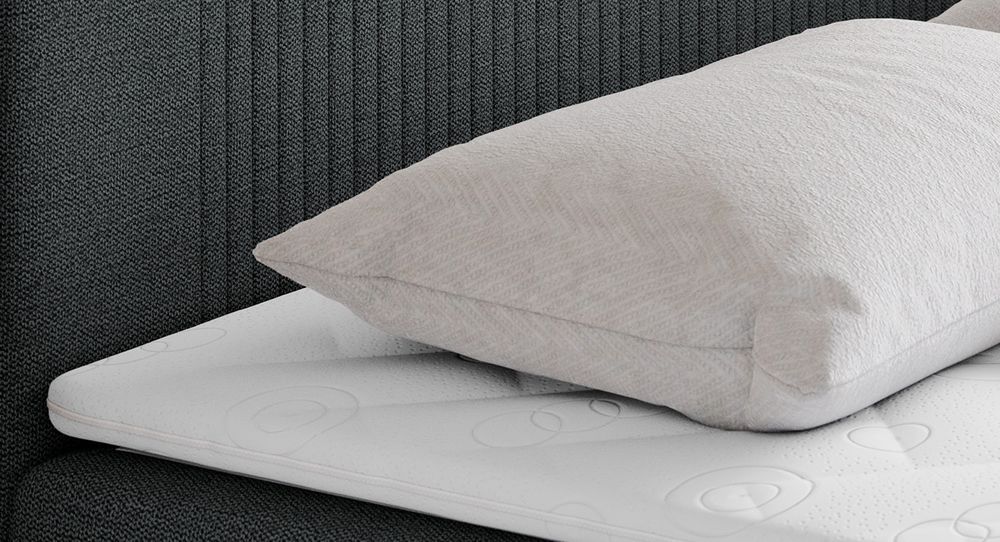 Gestepptes Kopfteil eines dunkelgrau Bettes. Eine Topper-Matratze liegt auf dem Bett