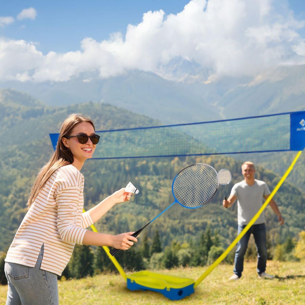 Frau spielt Badminton mit lächelndem Mann im Hintergrund, Berge im Hintergrund