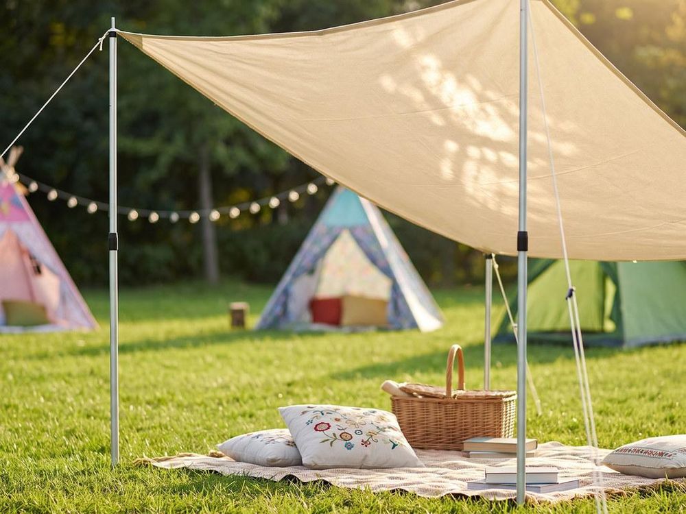 Sonnensegel über einer Picknickdecke auf der Wiese, gehalten von Aufstellstangen