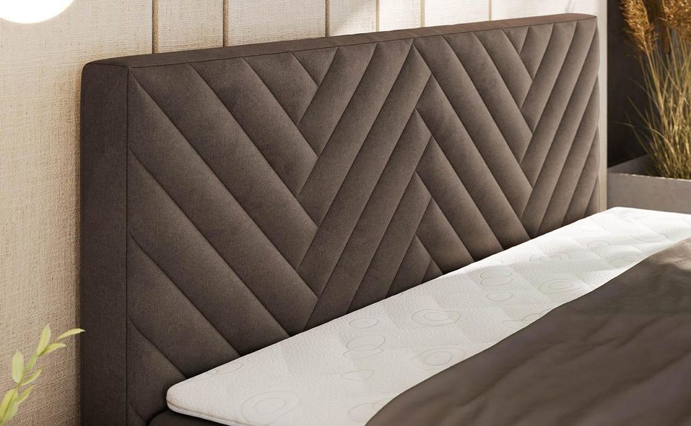 Detailansicht eines grauen Boxspringbetts mit gepolstertem Kopfteil im geometrischen Steppmuster.