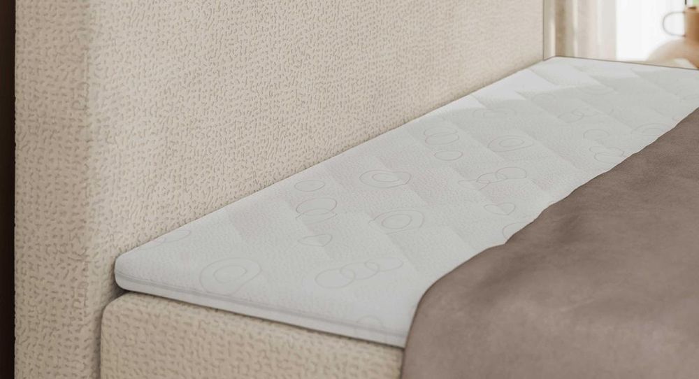 Gestepptes Kopfteil eines beigen Bettes. Eine Topper-Matratze liegt auf dem Bett