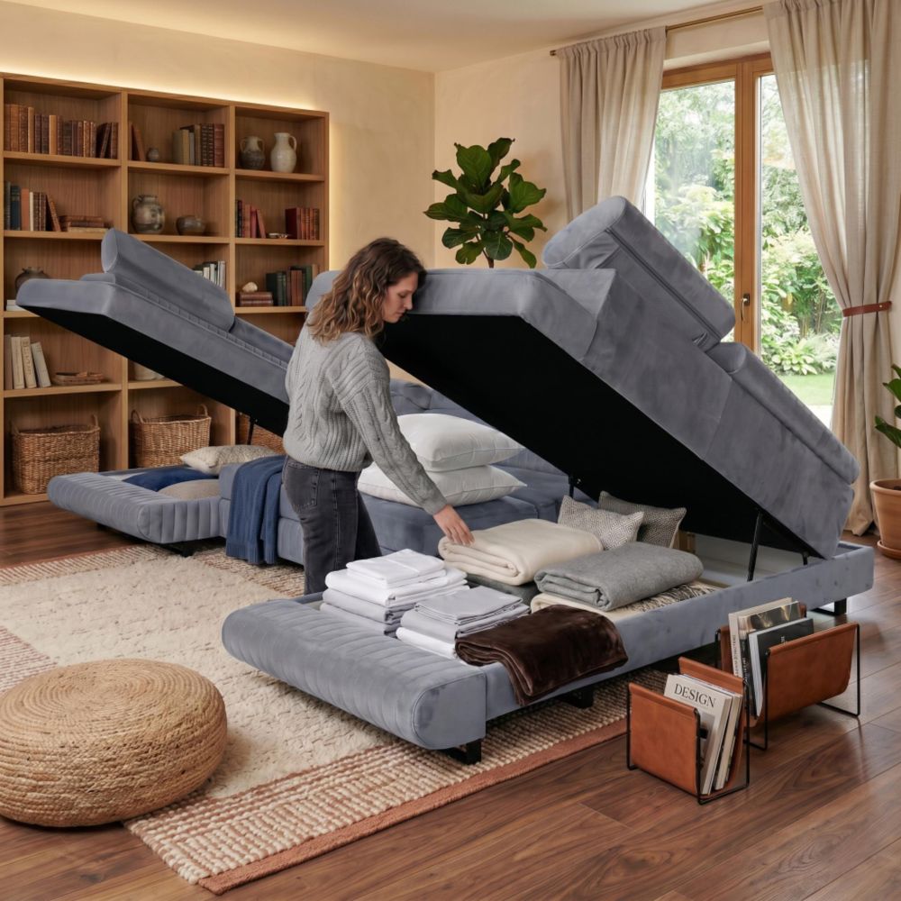Frau öffnet Bettkasten des Ecksofas. Innen gefaltete Bettwäsche, Kissen und Decken sichtbar.