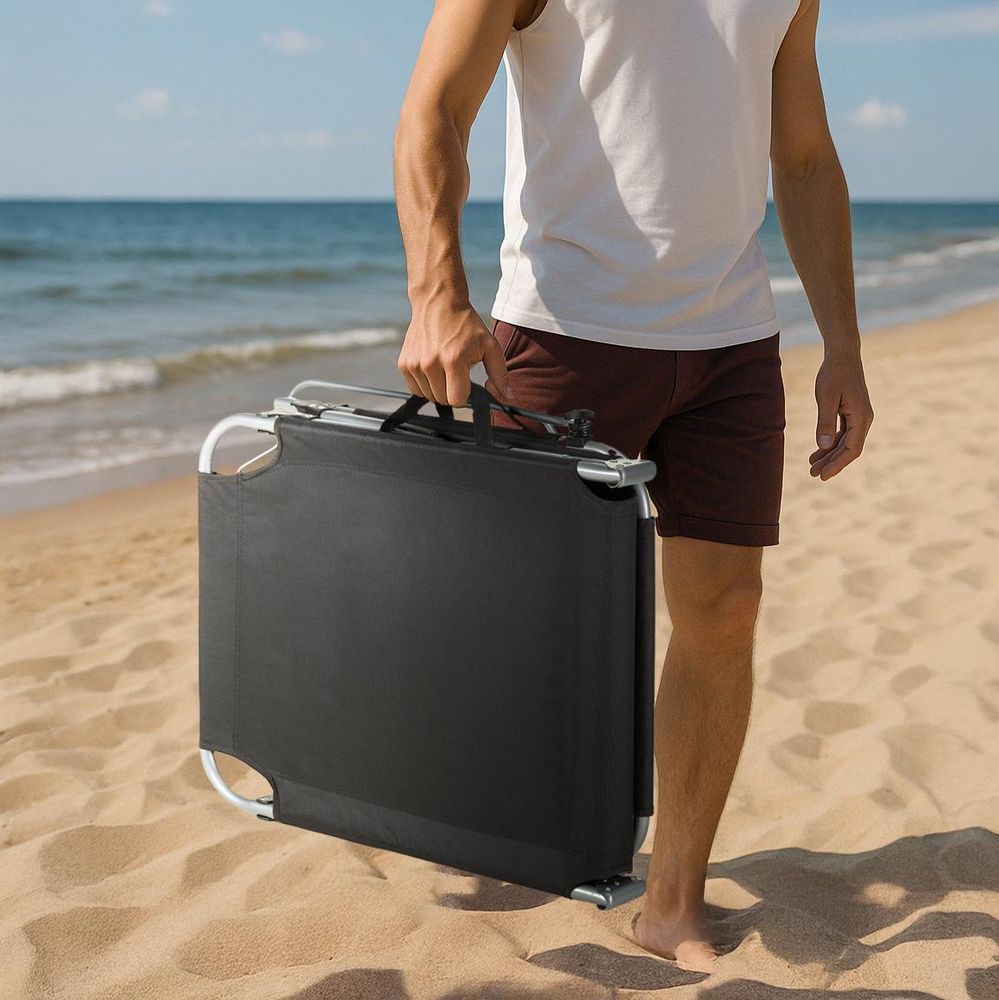 Ein Mann trägt die leichte, zusammengeklappte Sonnenliege am Griff über den Strand