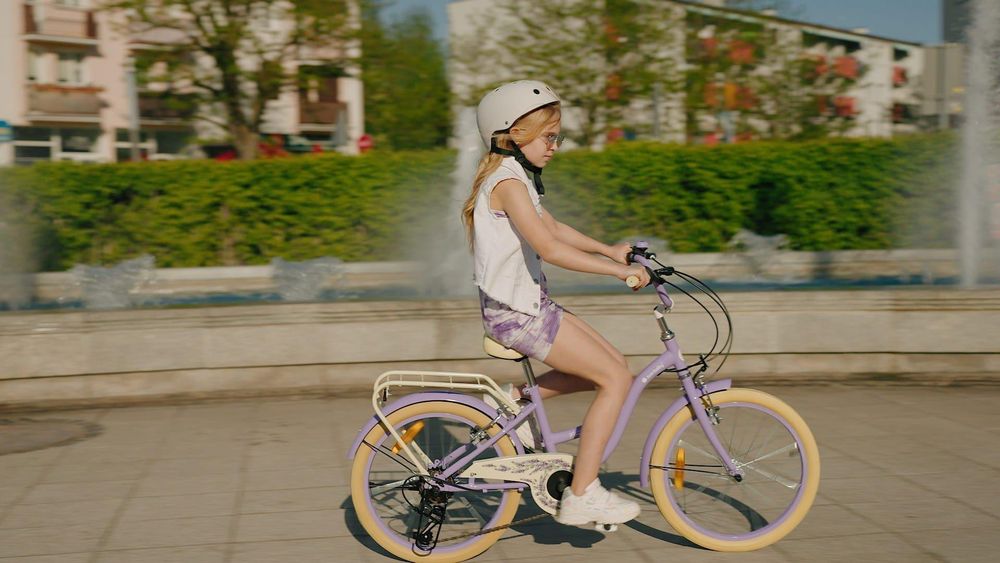 Niña montando la bicicleta lavanda, demostrando ajuste y comodidad.