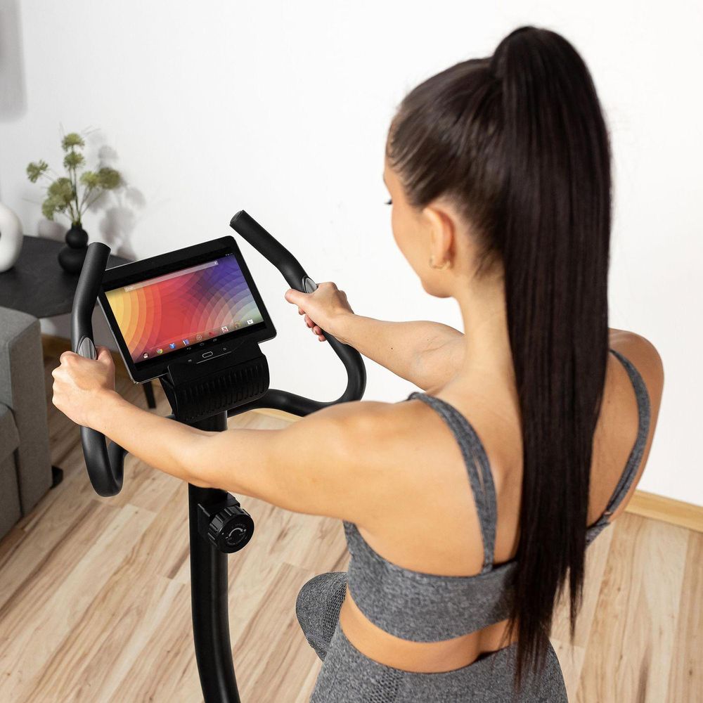 Rückenansicht der Frau, die trainiert, mit einem Tablet in der Halterung am Lenker des Heimtrainers