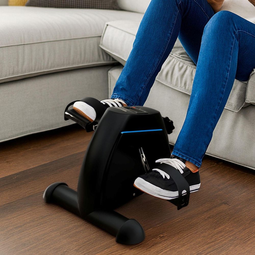 Nahaufnahme: Beine in Jeans und Sneakers auf Pedalen des Mini-Heimtrainers am Boden