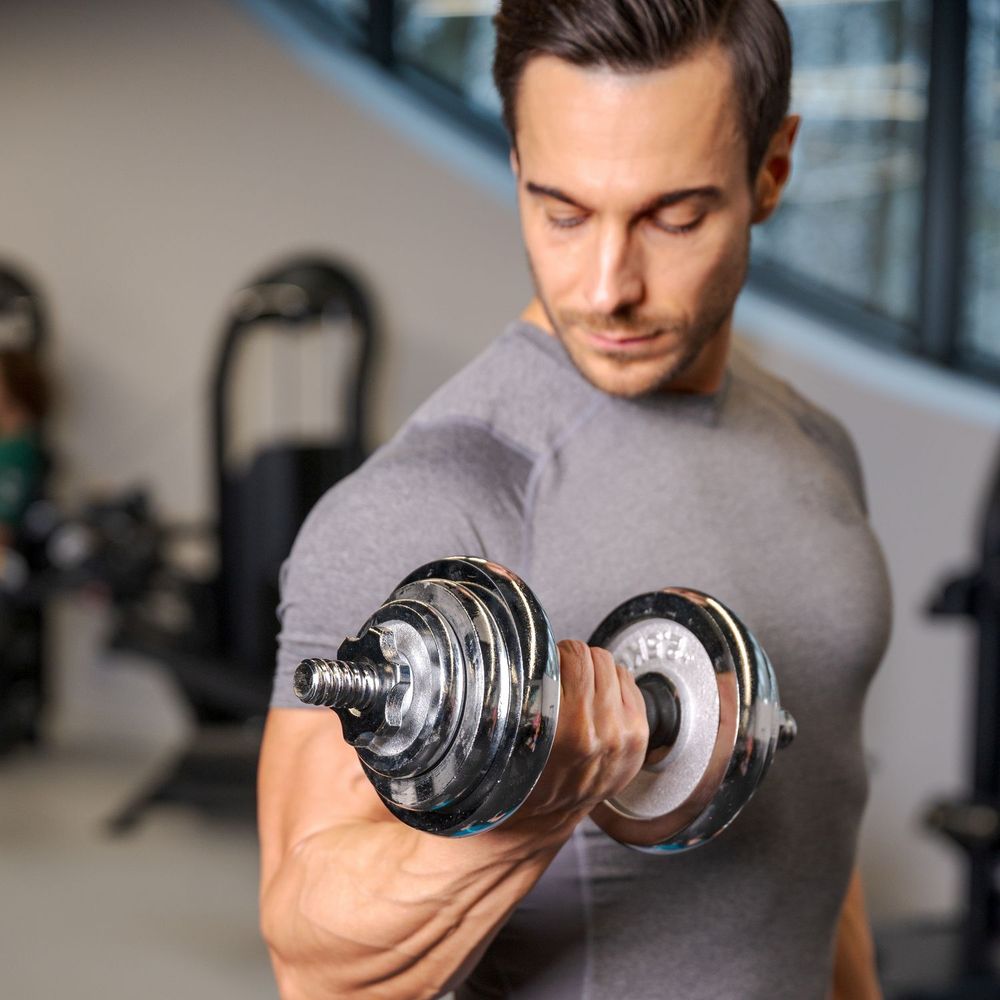 Mann trainiert Bizeps mit einer Kurzhantel im Fitnessstudio