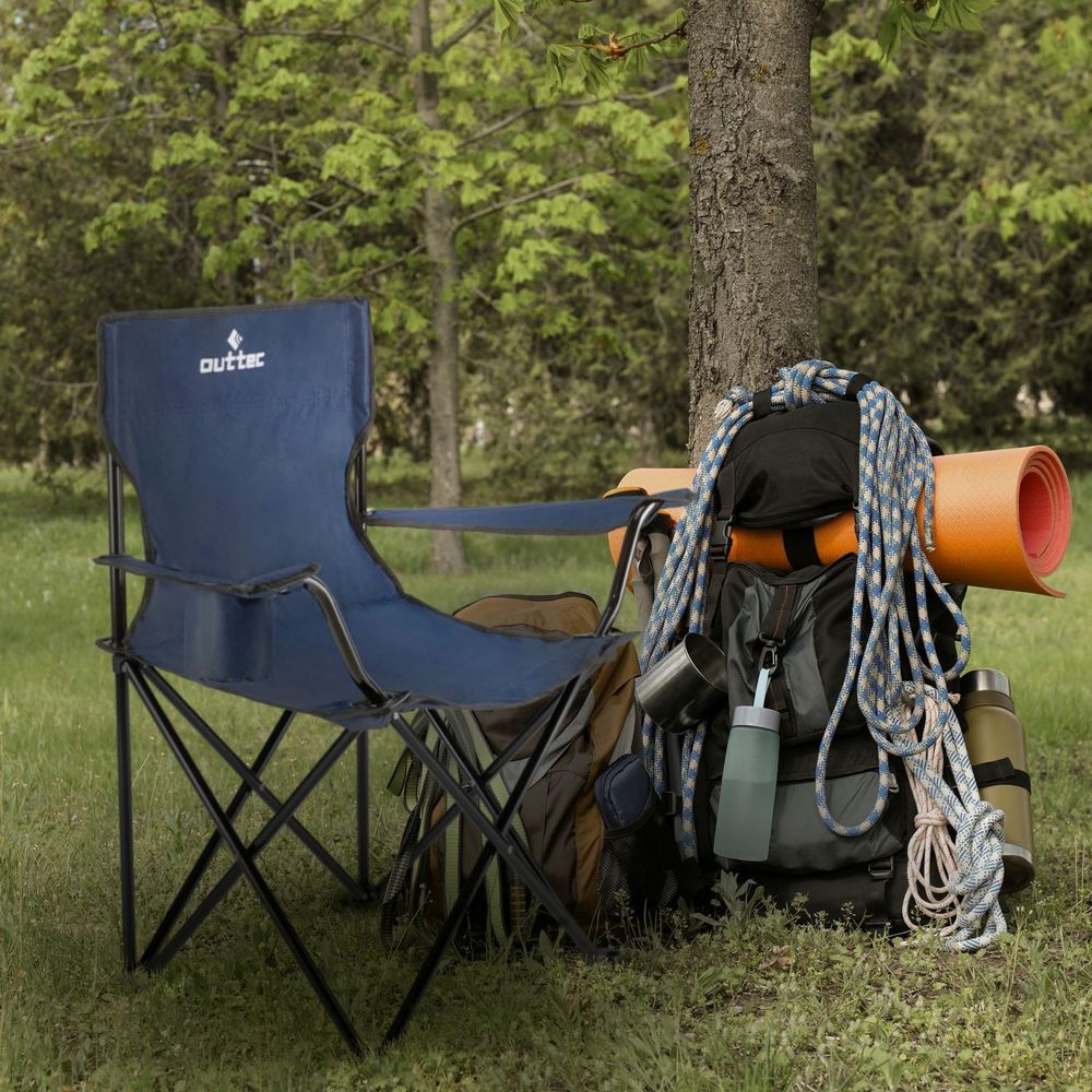 Blauer Campingstuhl neben Rucksack und Ausrüstung unter einem Baum.