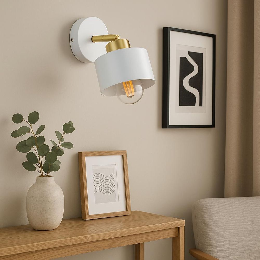 Weiße Wandleuchte mit goldenen Details über Holzkonsole mit Vase und gerahmten Bildern.