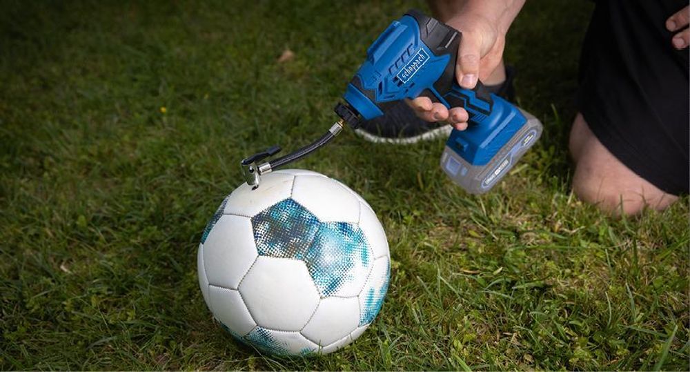 Das Bild zeigt den Handkompressor beim Aufblasen eines Fußballs.