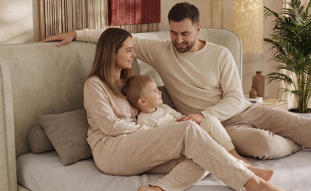 Familie spielt gemeinsam auf beigem Polsterbett im warmen Schlafzimmer.