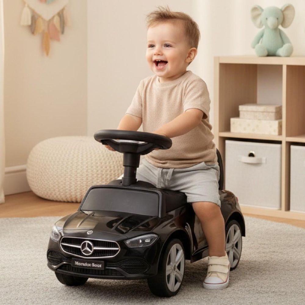 Enfant jouant sur le porteur Mercedes noir dans une chambre.