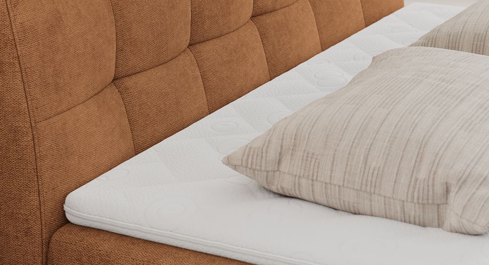 Gestepptes Kopfteil eines orange Bettes. Eine Topper-Matratze liegt auf dem Bett