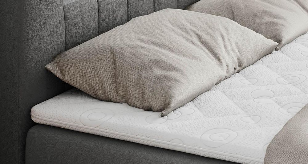 Gestepptes Kopfteil eines grau Bettes. Eine Topper-Matratze liegt auf dem Bett