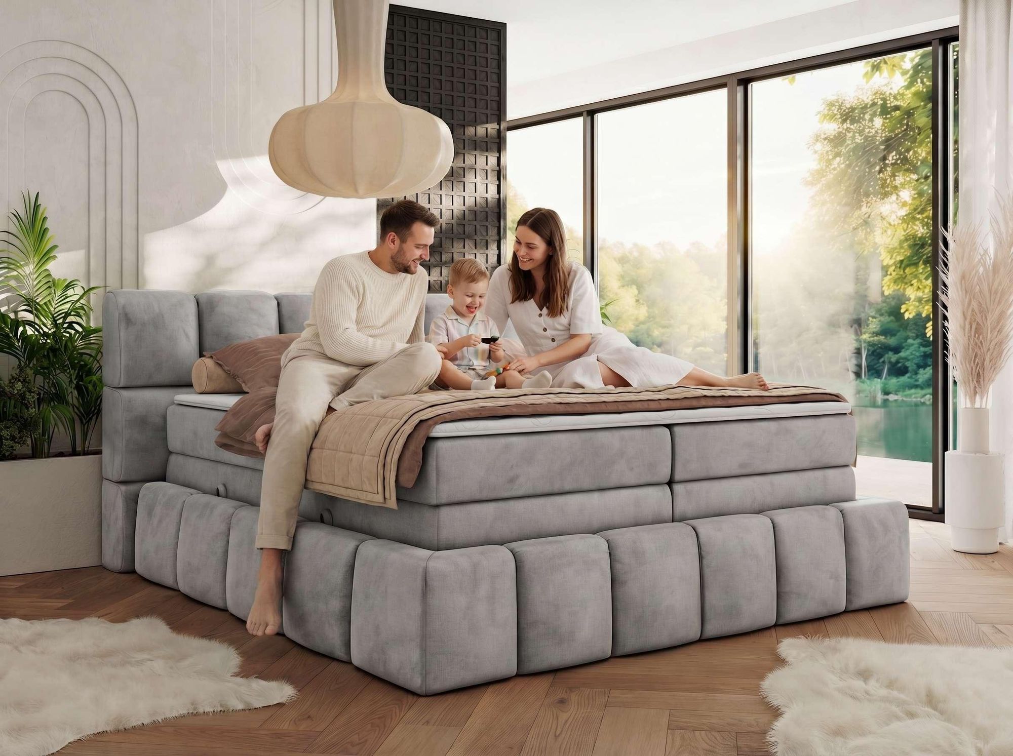 Familie entspannt auf grauem Boxspringbett im hellen Schlafzimmer.