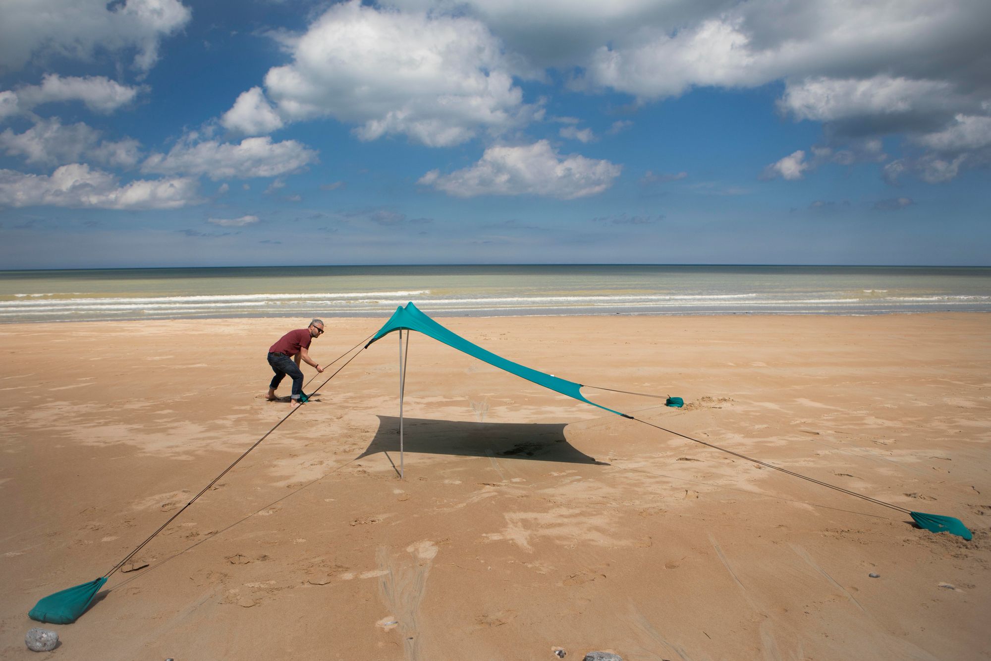 Das Bild zeigt, wie ein Mann das Strandzelt aufstellt