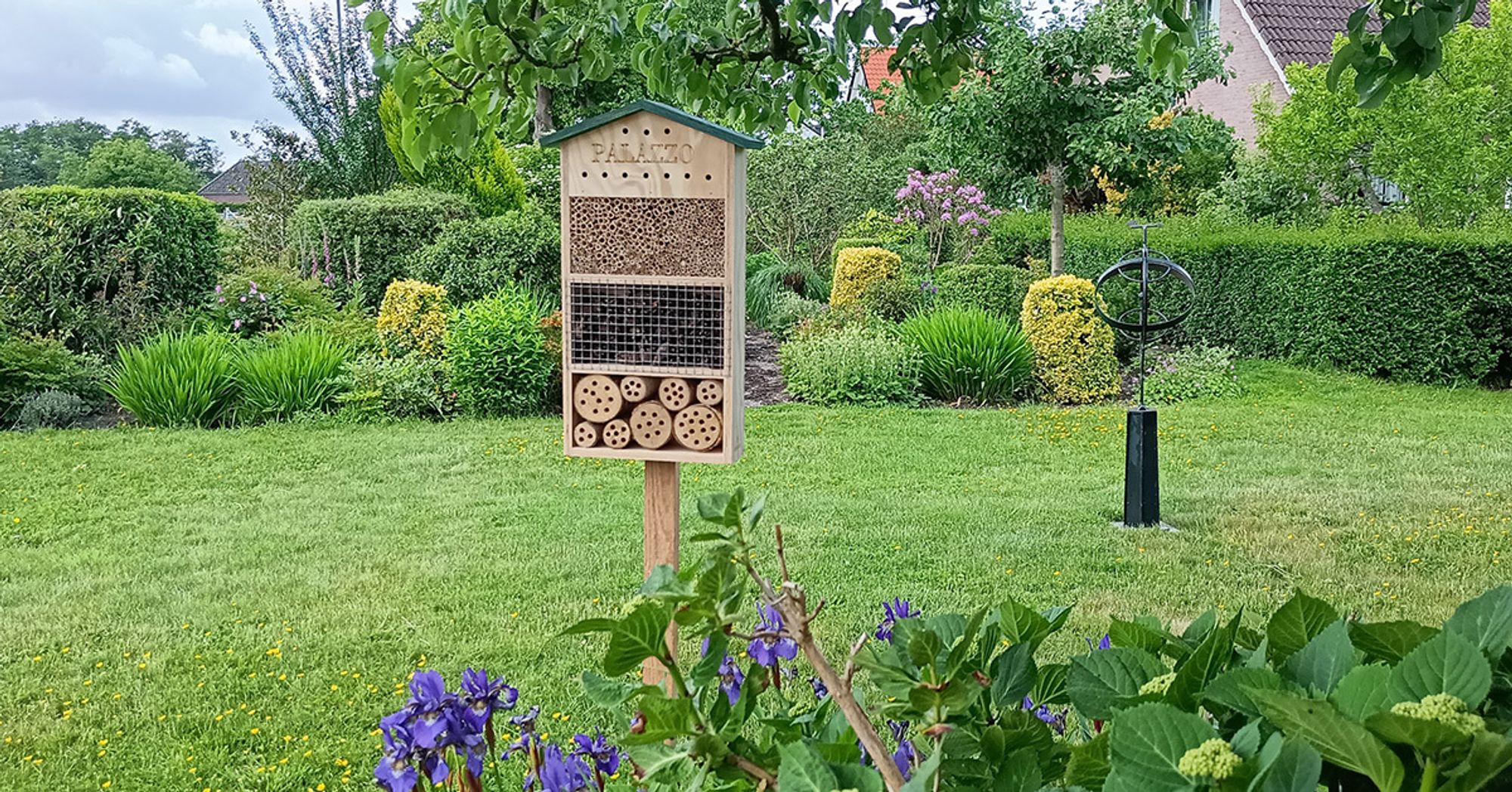 Insektenhotel "Palazzo" in einem Garten mit Gras und Blumen – ideal für Bienen und Marienkäfer.
