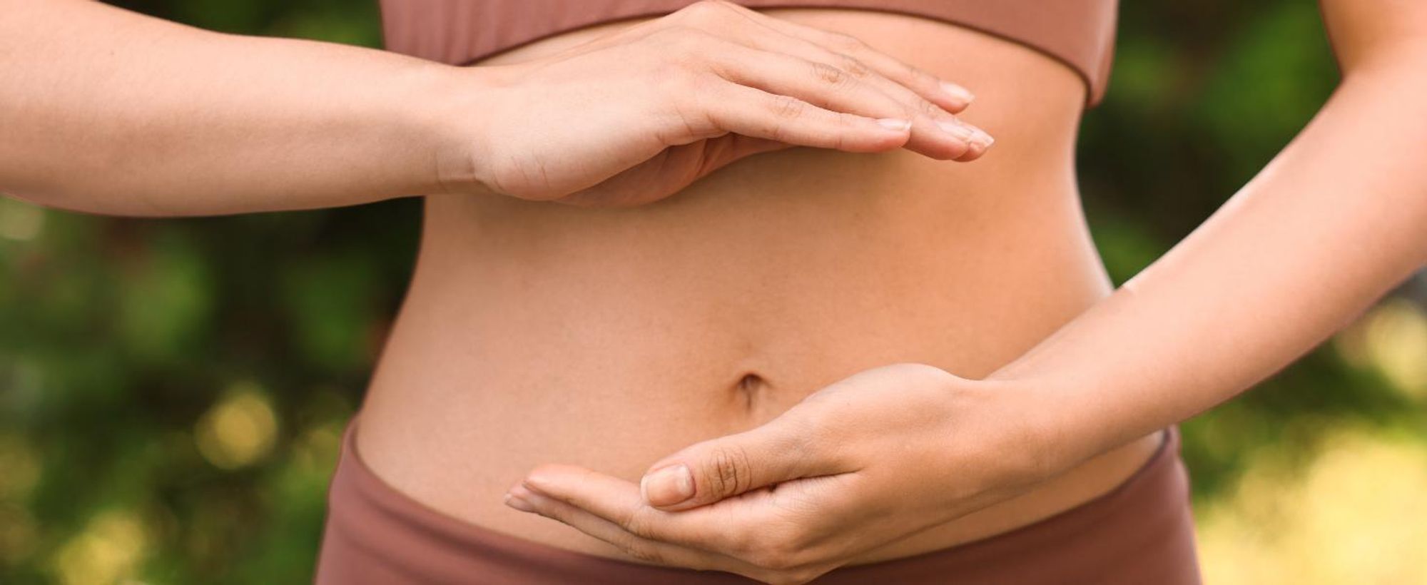Frau die ihre Hände sanft vor ihrem flachen Bauch hält