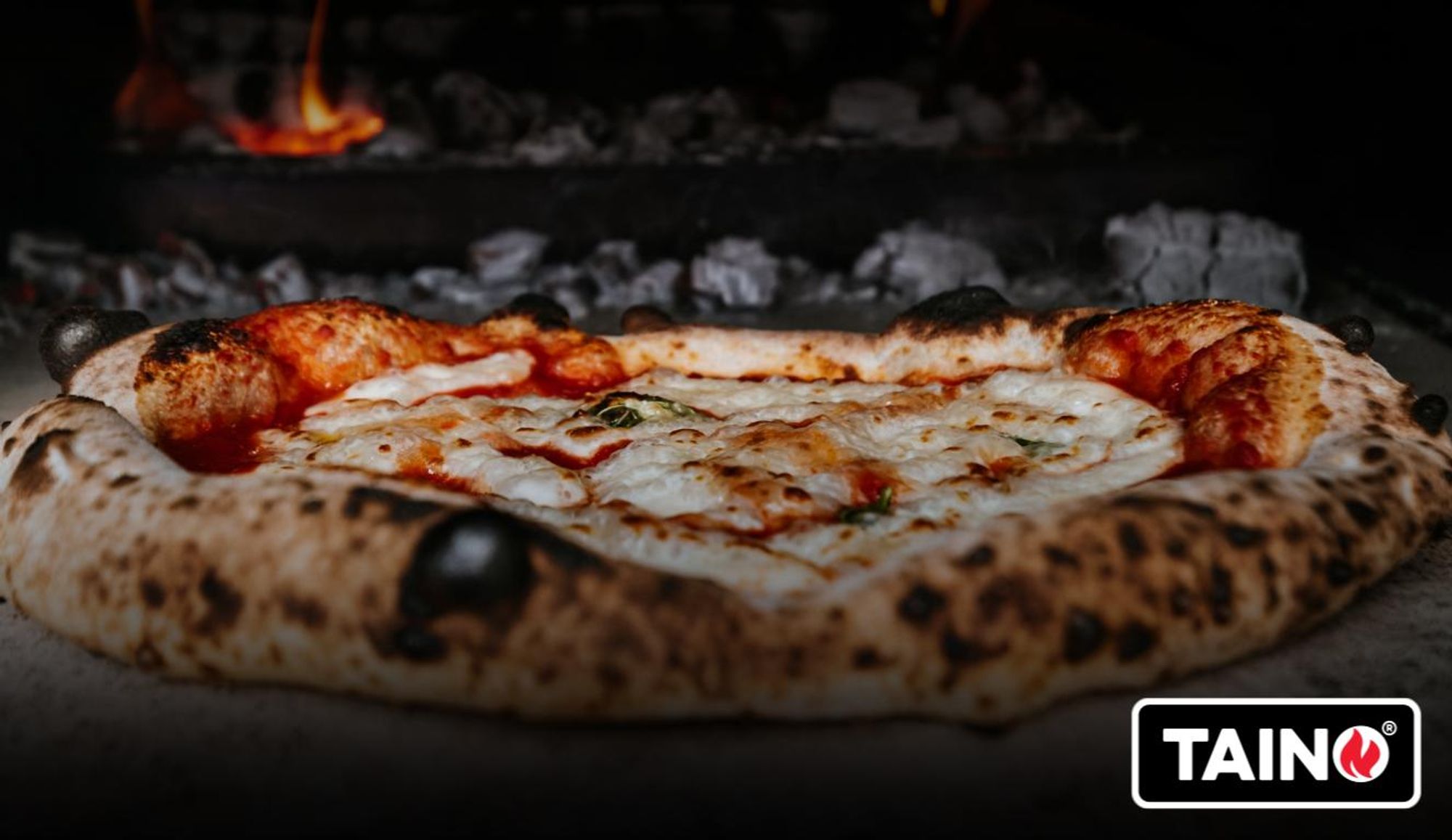 Fertig gebackene Pizza, im Hintergrund glühende Holzkohle
