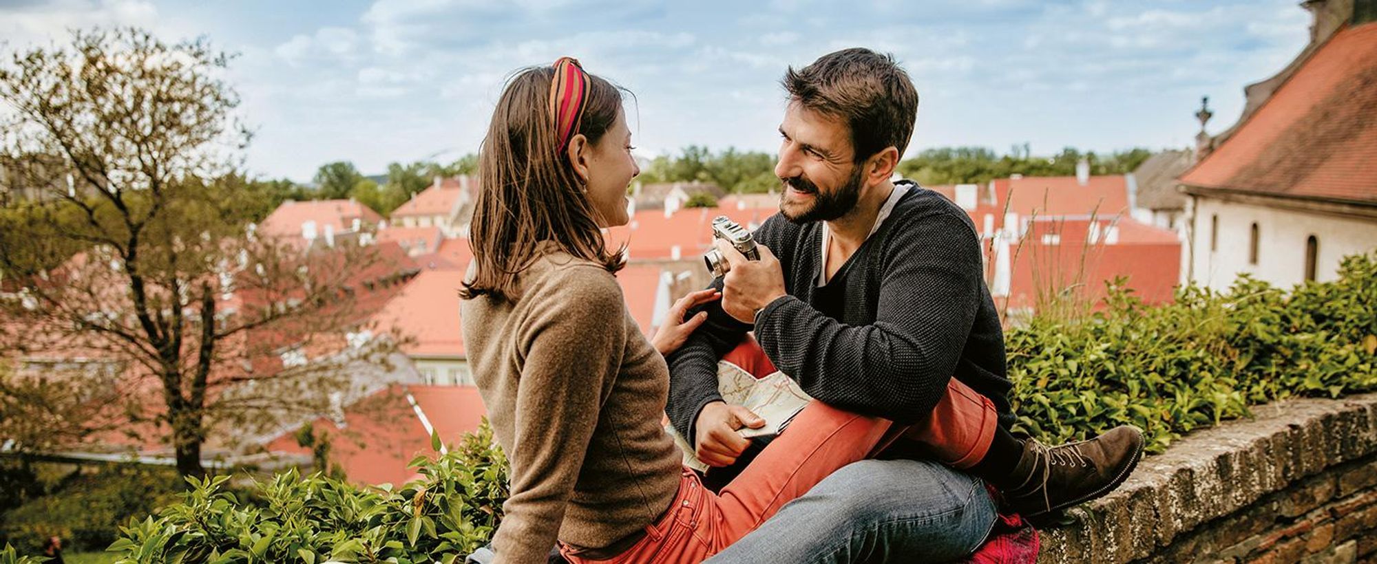 Das Bild zeigt ein lachendes Paar, das auf einer Mauer sitzt.