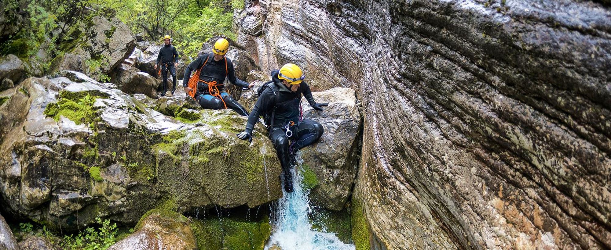 Das Bild zeigt drei Personen beim Klettern in einem kleinen Wasserfall.