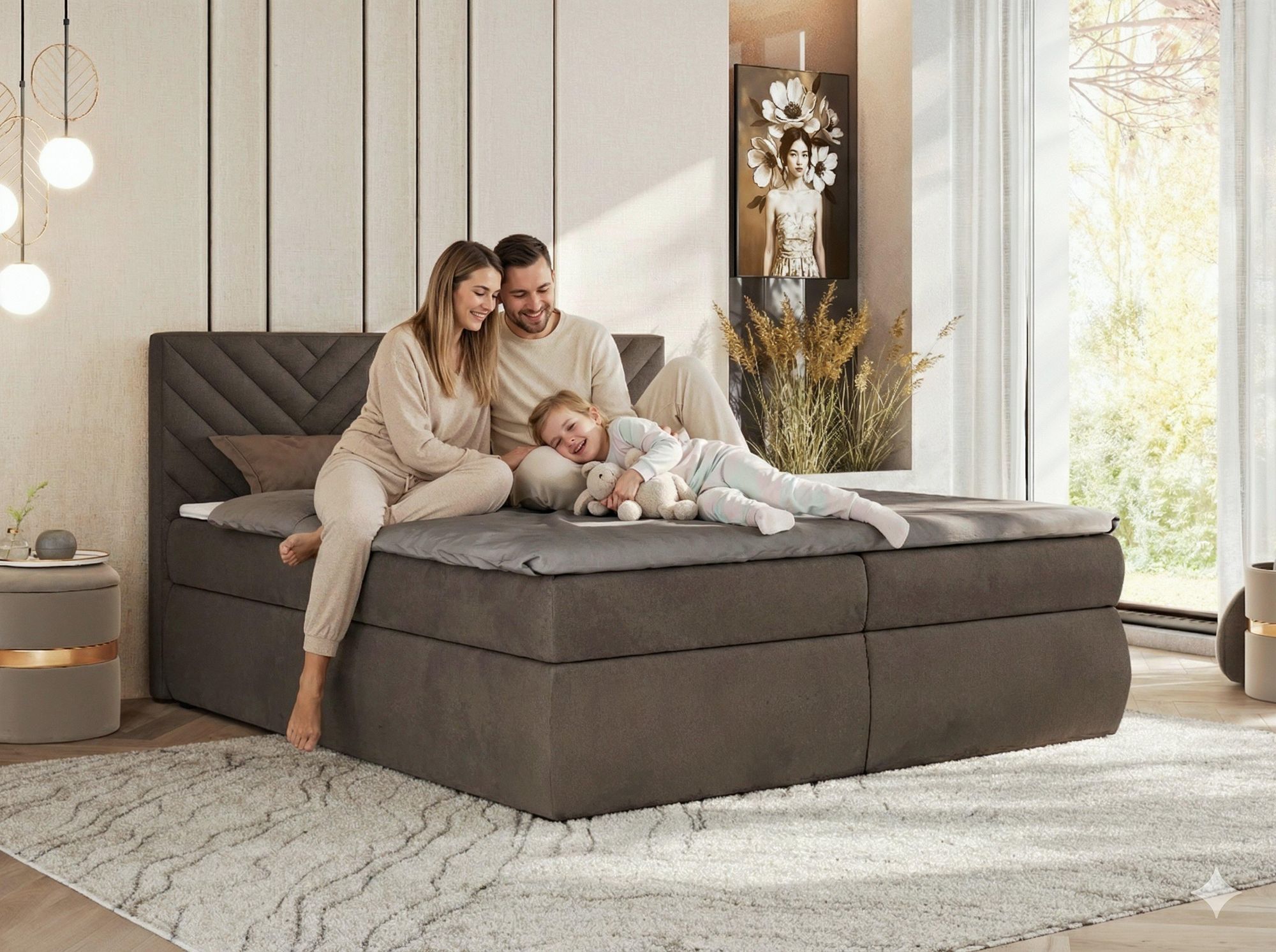 Familie entspannt auf grauem Boxspringbett im hellen Schlafzimmer.