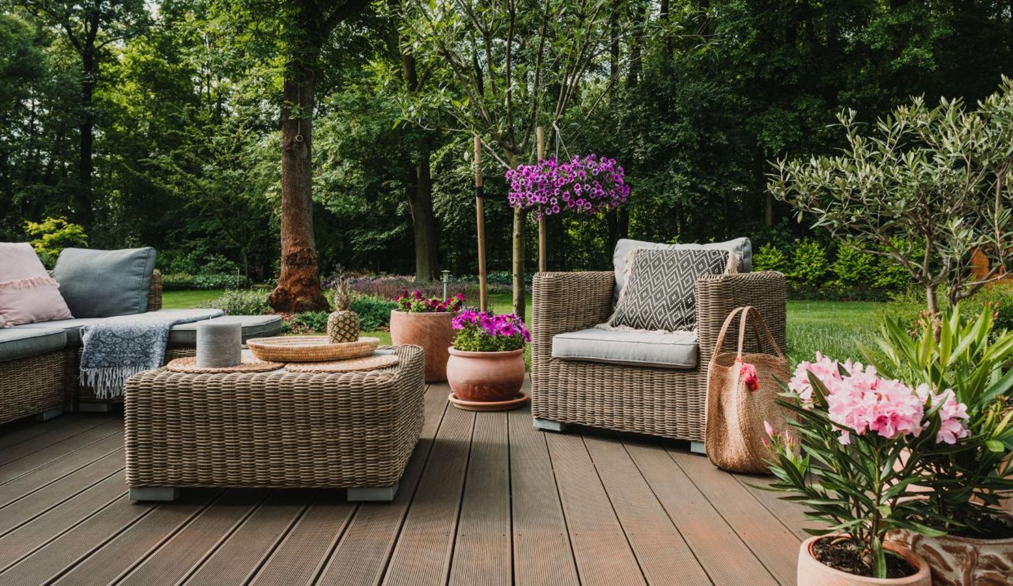 Terrasse mit Gartenlounge, Blumen und Bäumen im Hintergrund