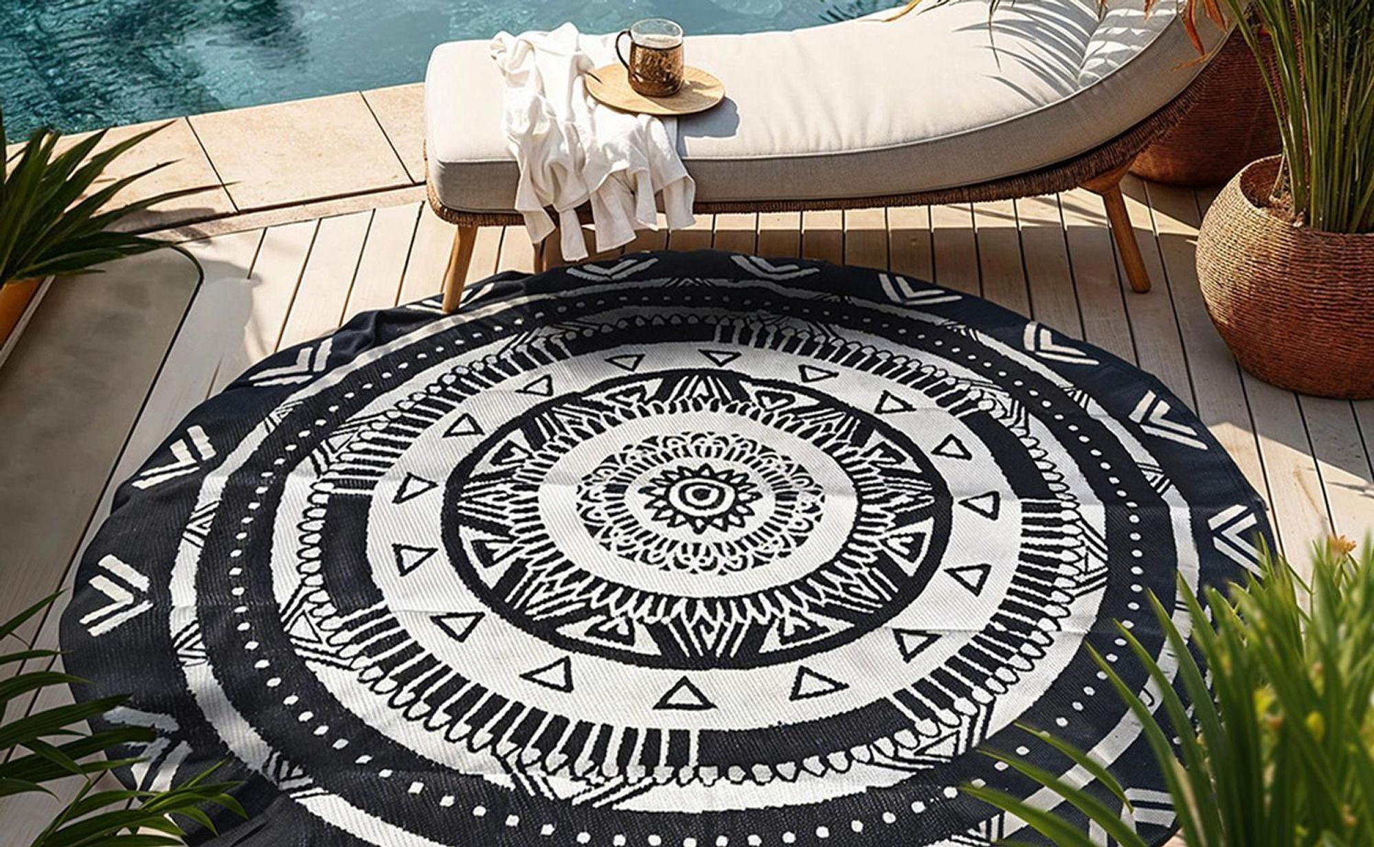 Runder schwarz-weißer Teppich mit Mandala-Muster auf einer Holzterrasse am Pool.